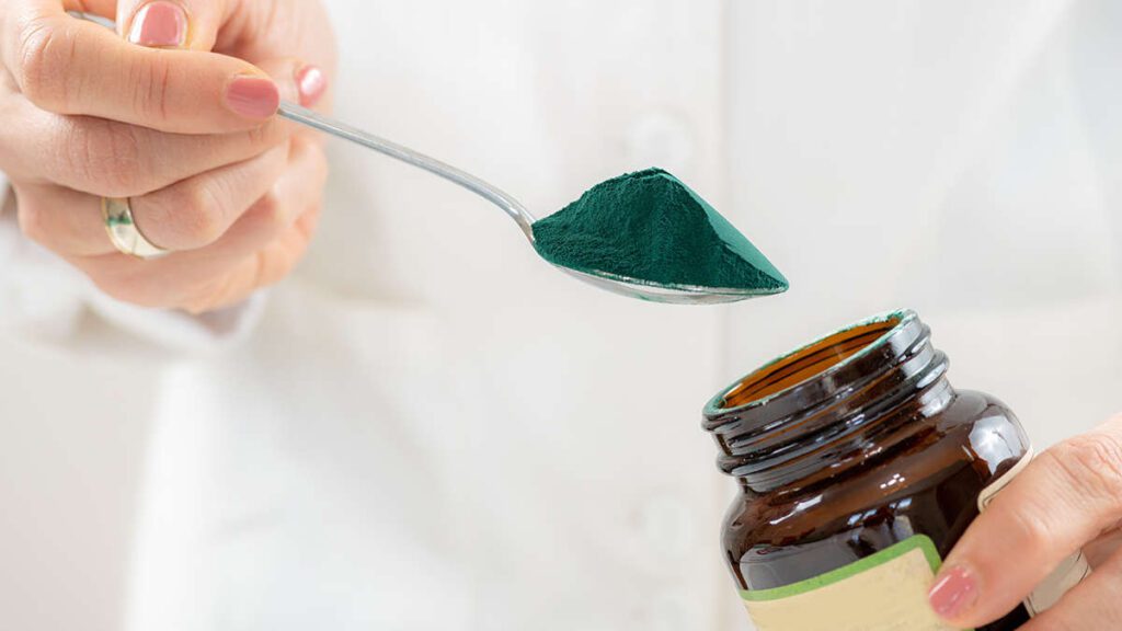 frau nimmt spirulina pulver aus einem glas